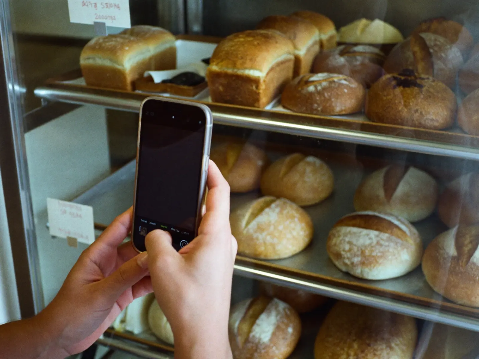Funcionária fotografando a vitrine de pães recém-abastecida com o celular